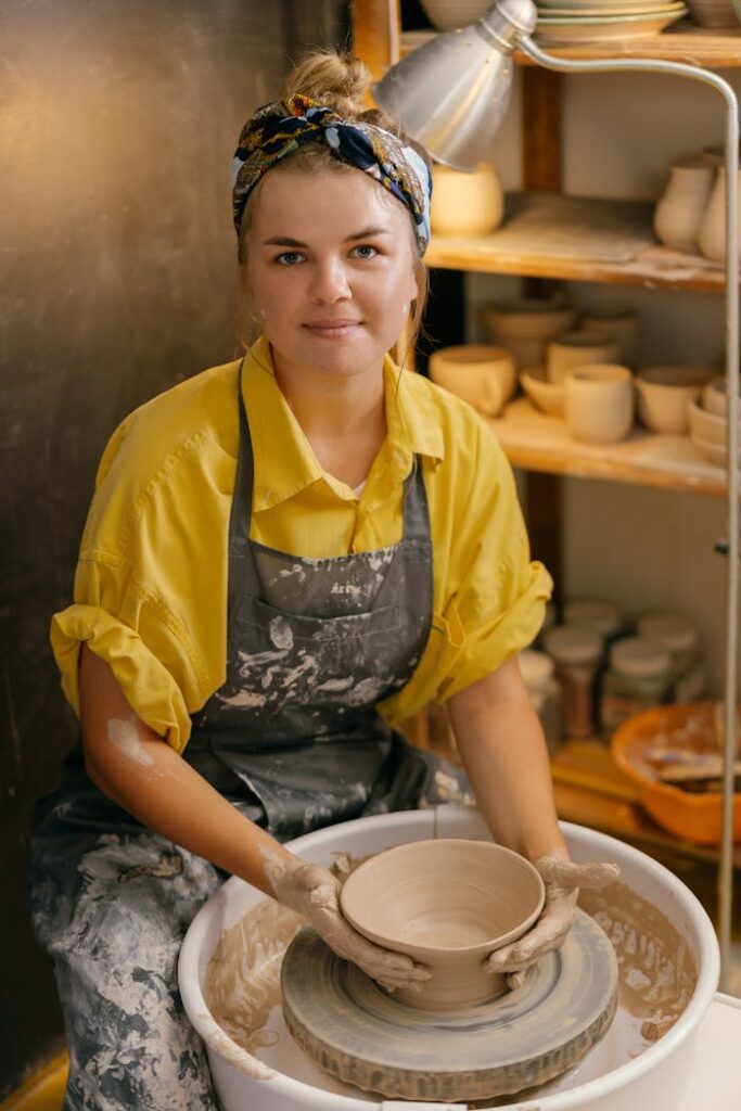 Female potter shaping clay on a wheel in an artisan studio, showcasing handmade pottery process.